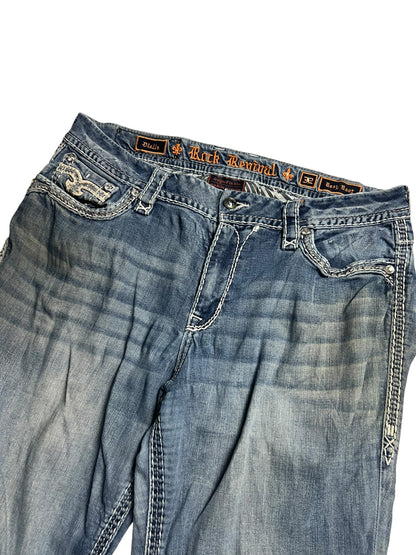 Ein Paar Rock Revival Mid Rise Boot Jeans von ZAZA resell, Größe 32 (XL), in blau mit weißen Nähten, dekorative Gesäßtaschen, abgenutzte Oberschenkel, Außenbeinlänge 110 cm, Bundweite 46 cm, abgebildet auf einem weißen Hintergrund.
