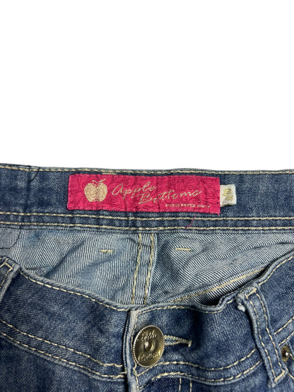 Nahaufnahme der Apple Bottoms Mid Rise Boot Jeans von ZAZA resell. Mit blauem Denim, rosa Apfel-Symbol-Etikett über dem Bund, sichtbarem Knopf, Nahtdetails und klarer Bundweite für einen klassischen Look.