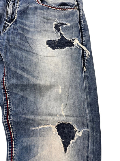 Nahaufnahme der True Religion Mega T Straight-Jeans von ZAZA resell in Größe 34 (M) mit starken Ausfransungen und Rissen an Oberschenkel und Knie, sichtbarem dunklem Unterstoff, detaillierten Nähten und rot-weiß-blauen Seitenstreifen.